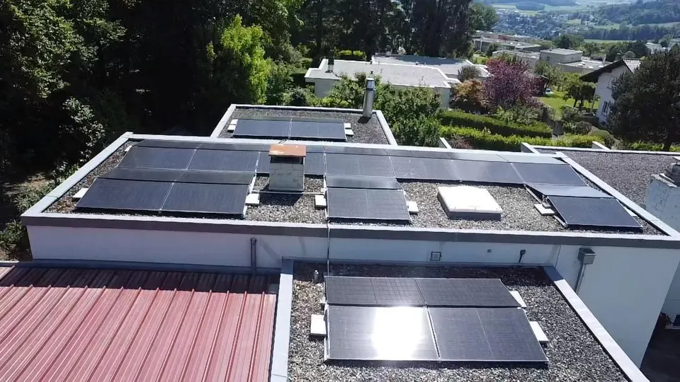 Vue aérienne : modules solaires noirs sur le toit plat d’une maison individuelle à Villars-sur-Glâne (environs : arbres)