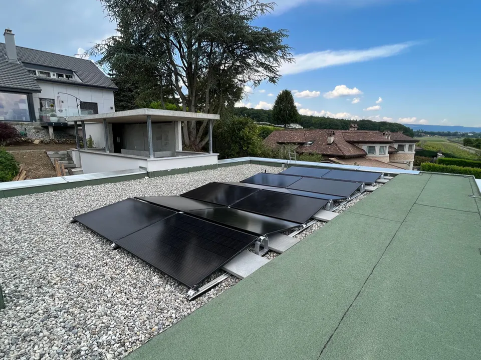 Modules solaires noirs sur le toit plat d’une maison individuelle à Crans-près-Céligny (environs : arbres)