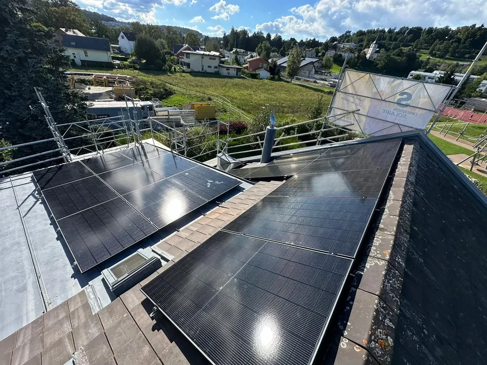 Schwarze Solarmodule auf dem grauen Ziegeldach eines Einfamilienhauses in Matran (Umgebung: Nachbarhäuser, Bäume)