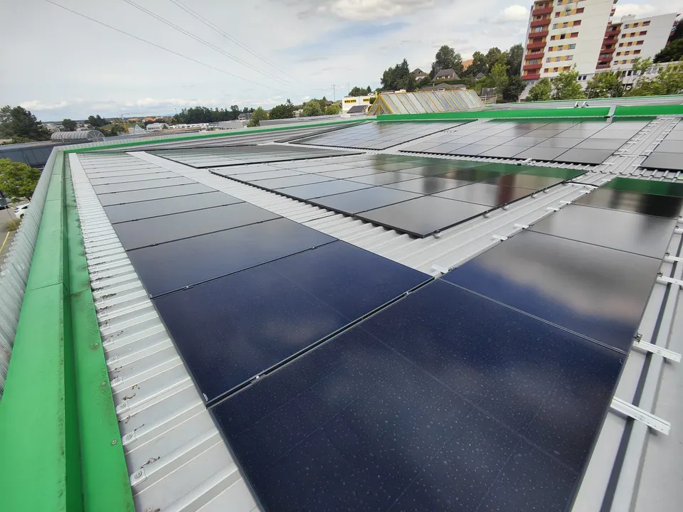 Schwarze Modulreihen auf dem Blechdach des Gewerbegebäudes in Givisiez, grüne Dachrandabdeckung, im Hintergrund Wohnhochhäuser