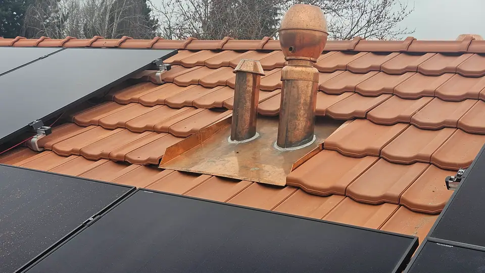 Détail : modules noirs à côté des sorties de toit en cuivre sur le toit en tuiles à Cottens