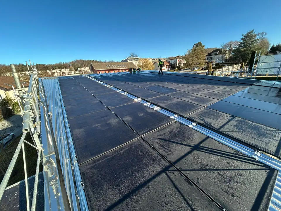 Phase de chantier : modules solaires noirs sur le toit en tôle d’un bâtiment public à Villars-sur-Glâne