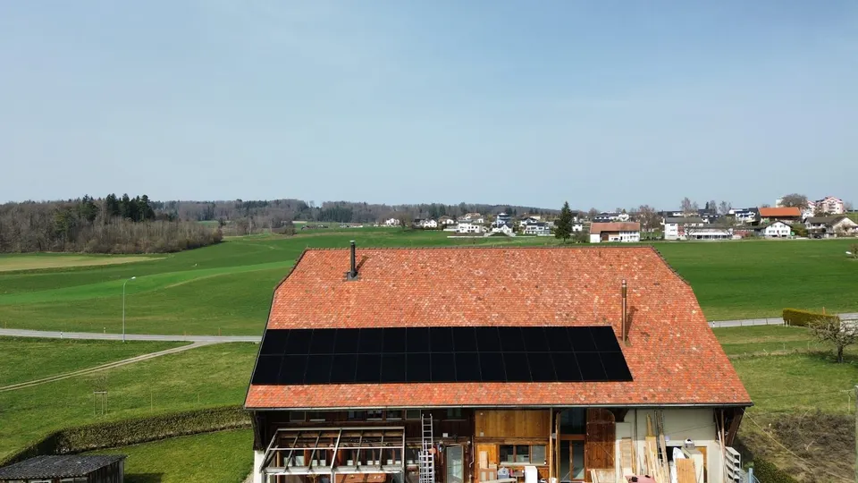 Luftbild: schwarze Solarmodule auf dem roten Ziegeldach eines Bauernhauses in Chénens (Umgebung: Wiesen) – weitere Ansicht