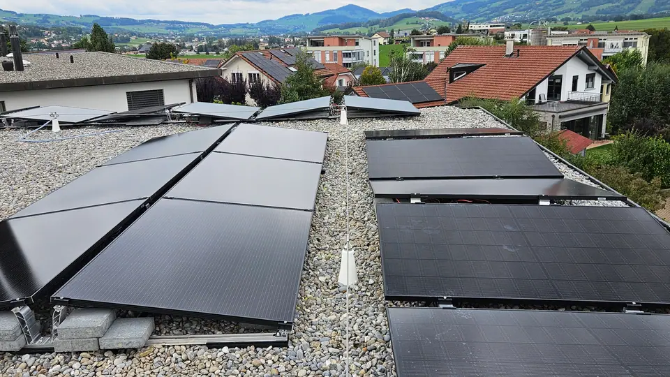 Deux rangées de modules noirs surélevés sur le toit gravillonné à Bulle, quartier résidentiel et Préalpes en arrière-plan