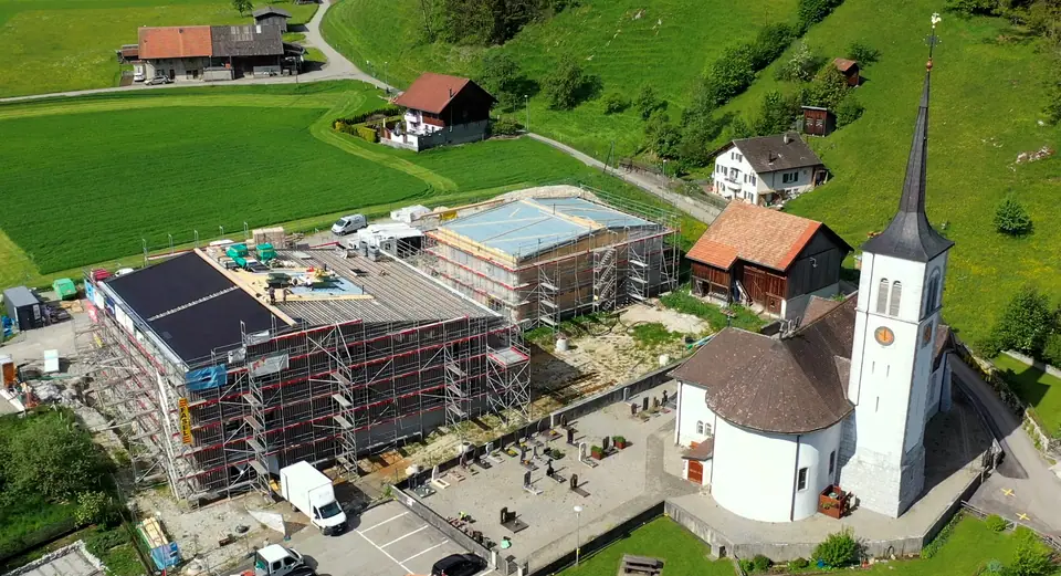 Vue aérienne : école de Neirivue avec toiture solaire intégrée noire à côté de l’église