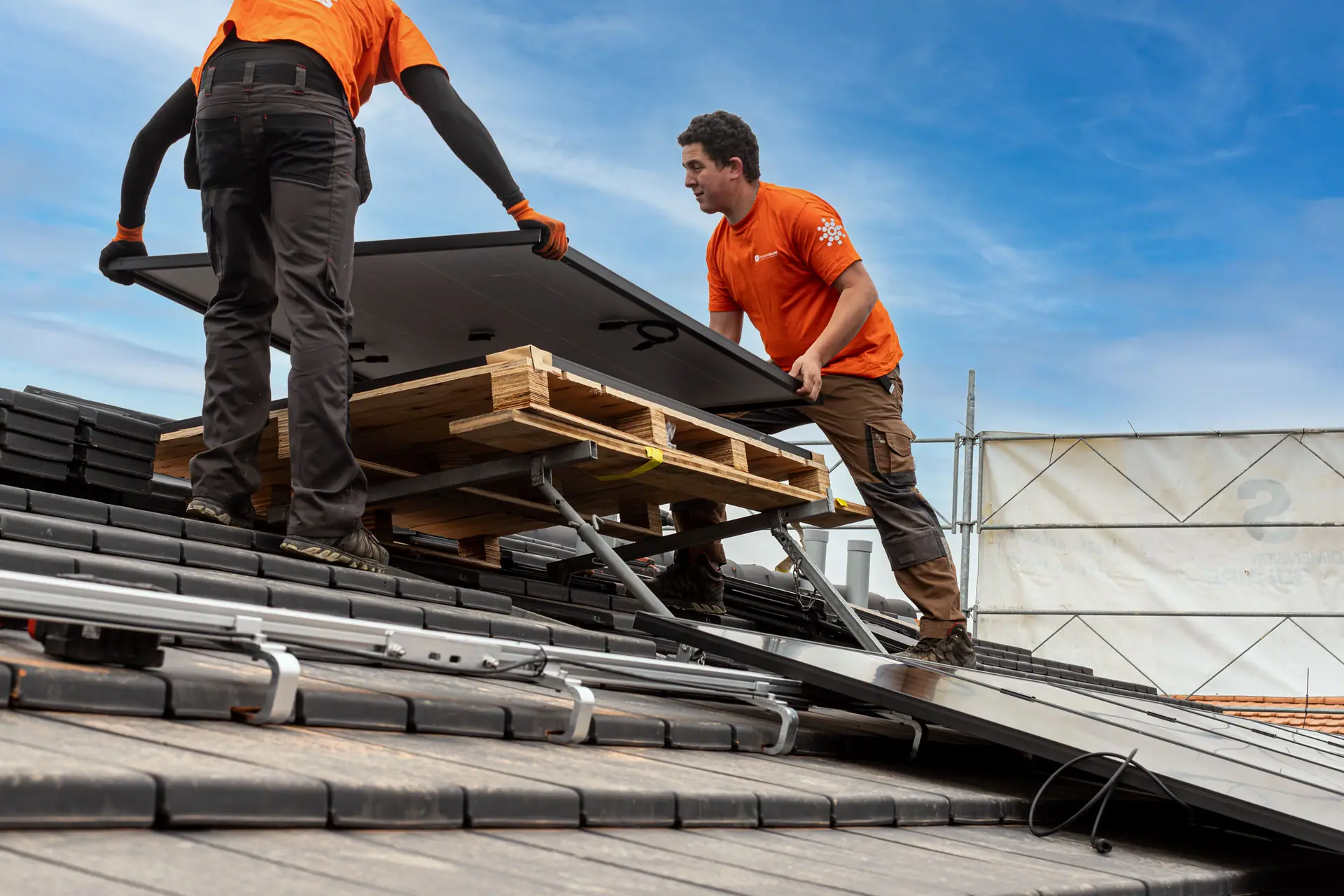 Deux monteurs de Dimension Solaire portent un module solaire sur un toit en tuiles